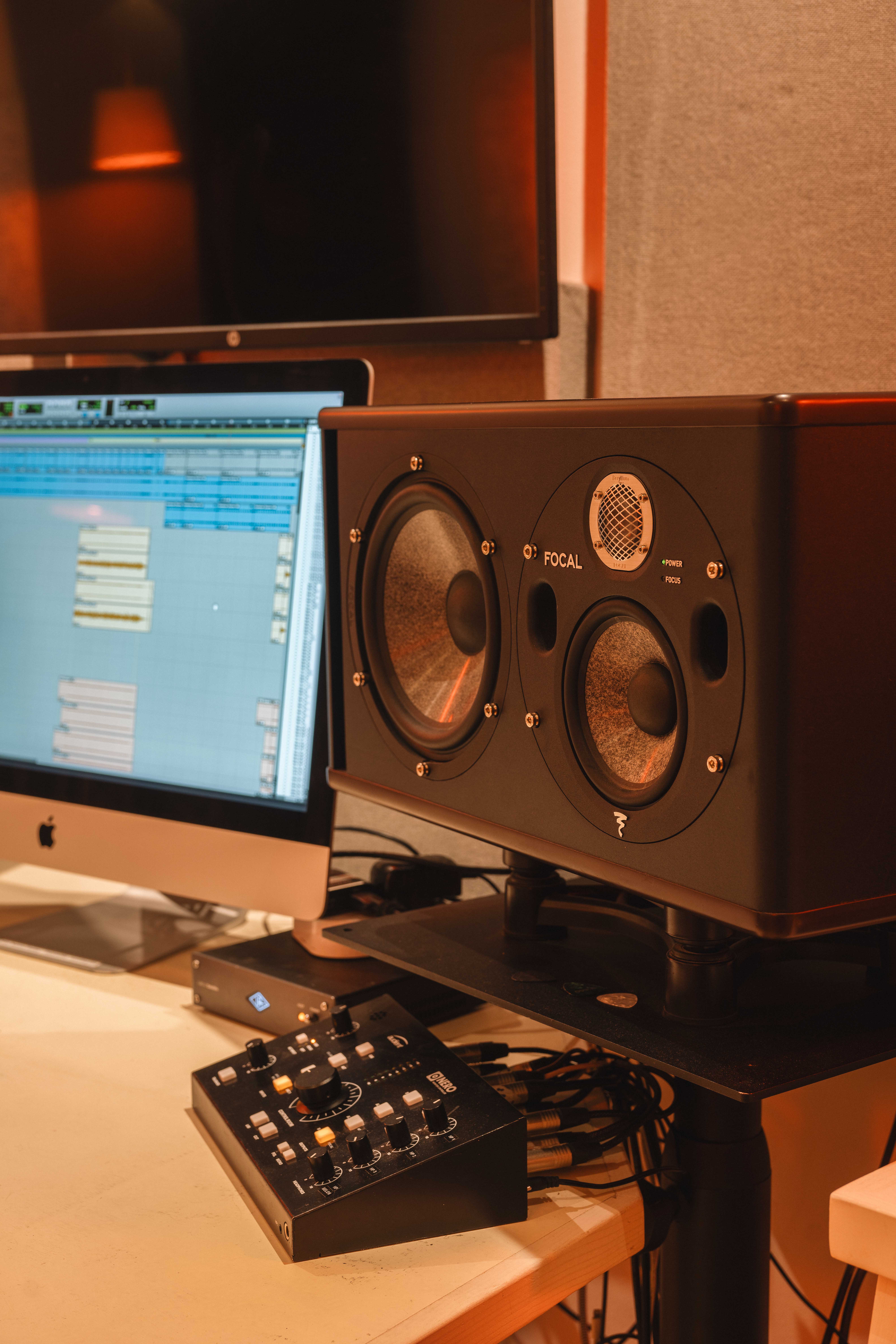 Close-up of a Focal studio monitor speaker next to a computer displaying audio editing software on a desk with audio control equipment.