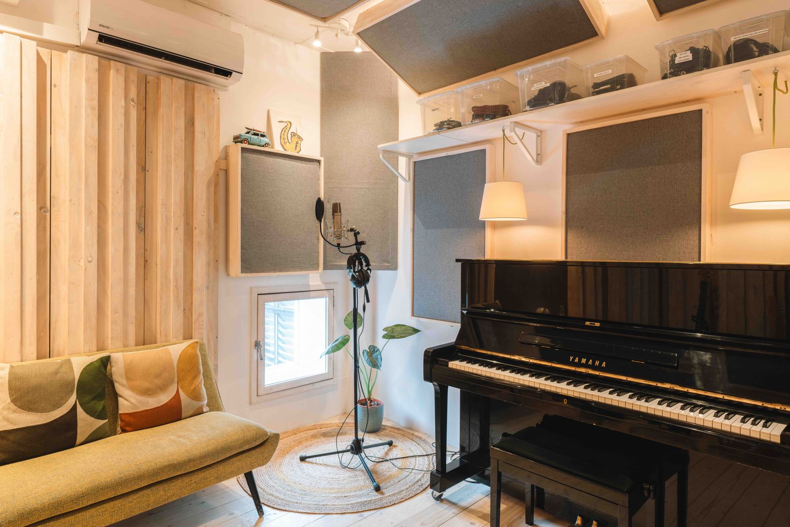 Cozy music studio with a black Yamaha piano, a microphone on a stand, a green sofa with patterned cushions, and acoustic panels on the walls.