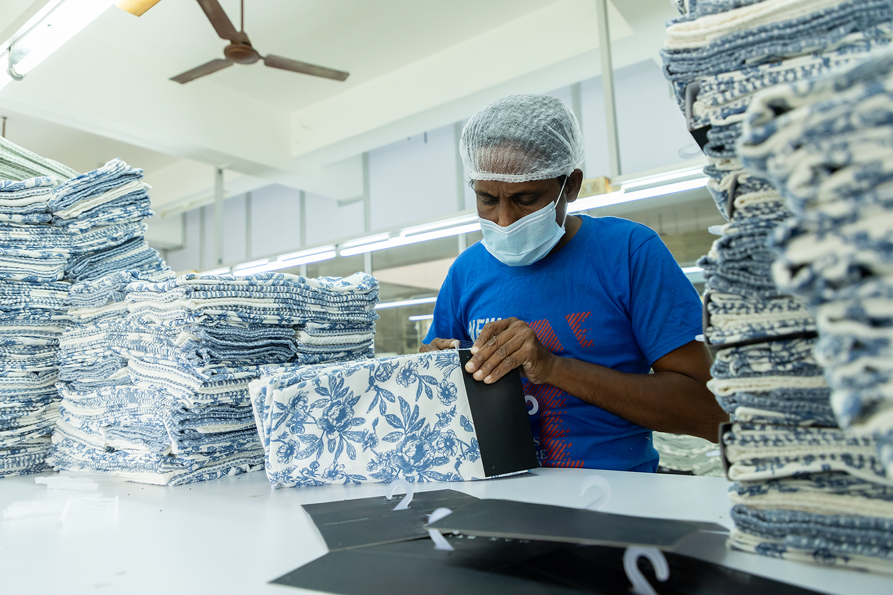 Worker in a hairnet and mask folding patterned fabric, from packing unit of  Anubav Fabrics, karur.

