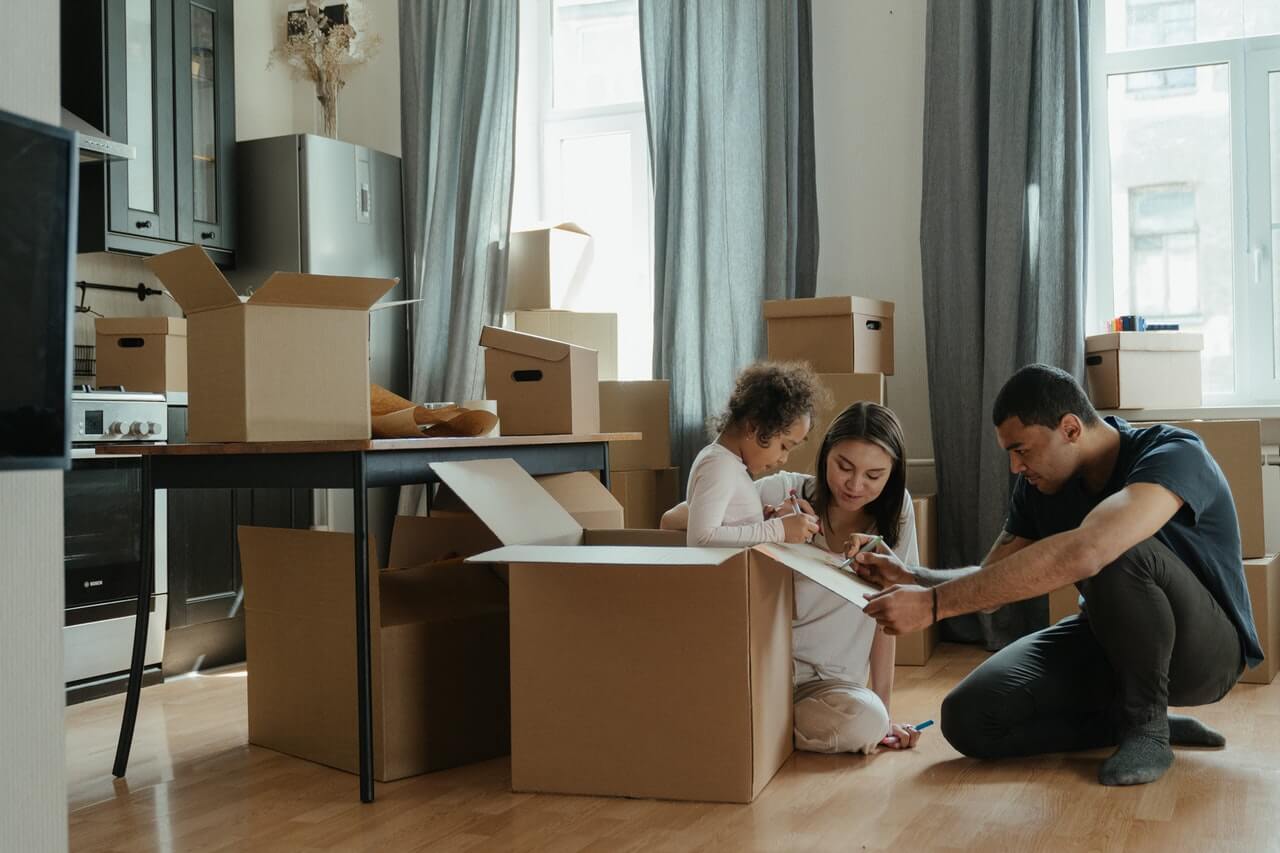 Image of a family sitting on the floor going over a moving checklist. They are surrounded by moving boxes with their home's items packed up as they prepare for their next move.