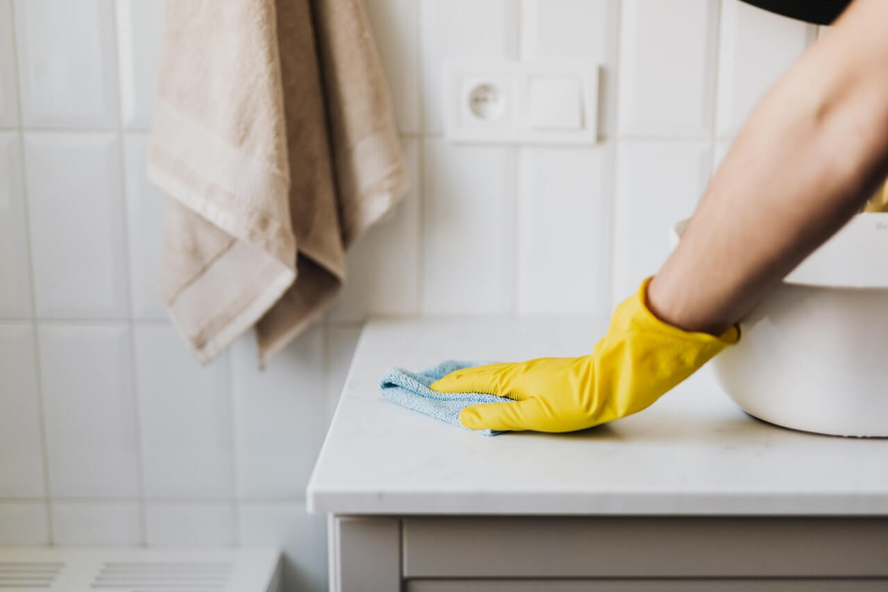 Image of a house cleaner wiping down a countertop with a gloved hand and a rag.