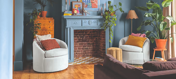 Cozy living room with blue-gray walls, a fireplace, armchairs, and houseplants
