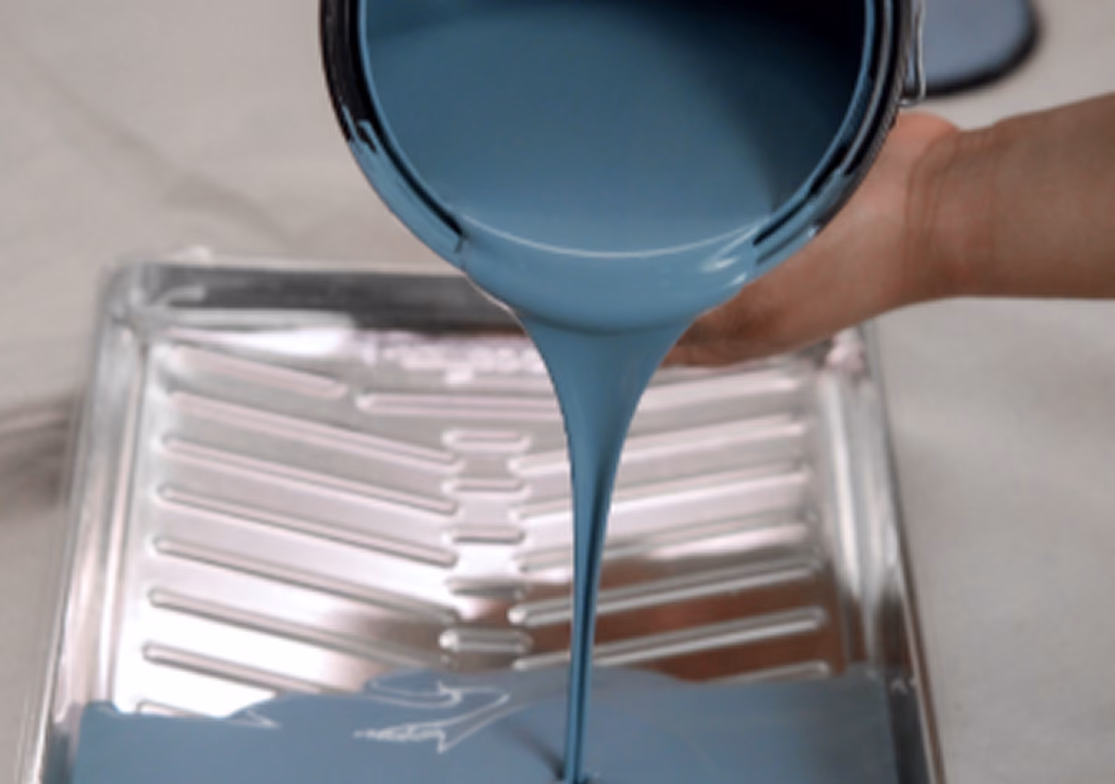 Gray-blue paint pouring from a can into a metal roller tray