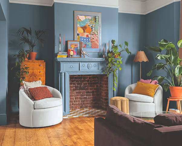 Cozy living room with blue-gray walls, a fireplace, armchairs, and houseplants