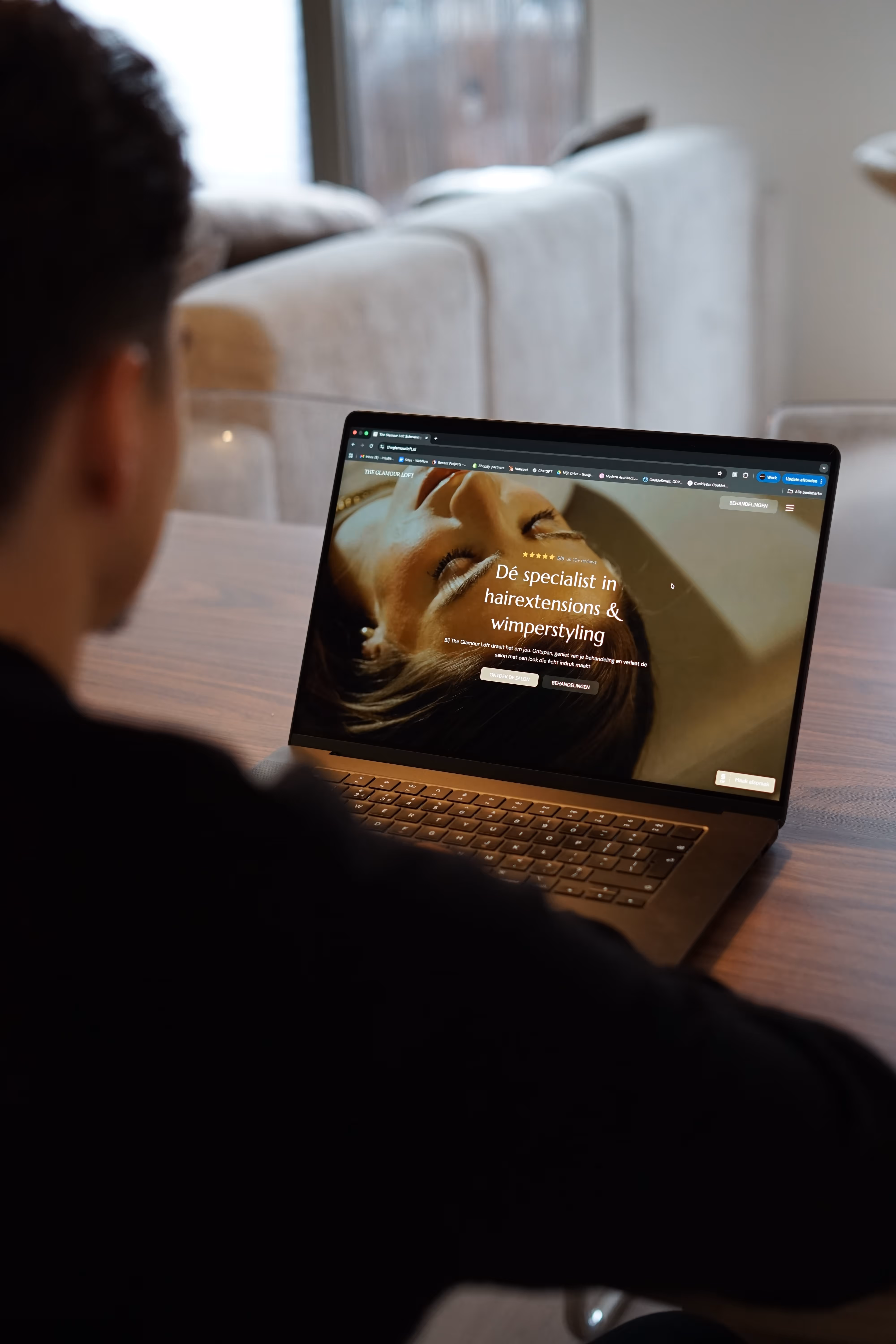 Person viewing a laptop displaying a website for hairextensions and wimperstyling with an image of a woman lying down.