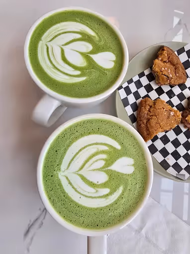 Two cups of matcha drinks with a sliced cookie on the side