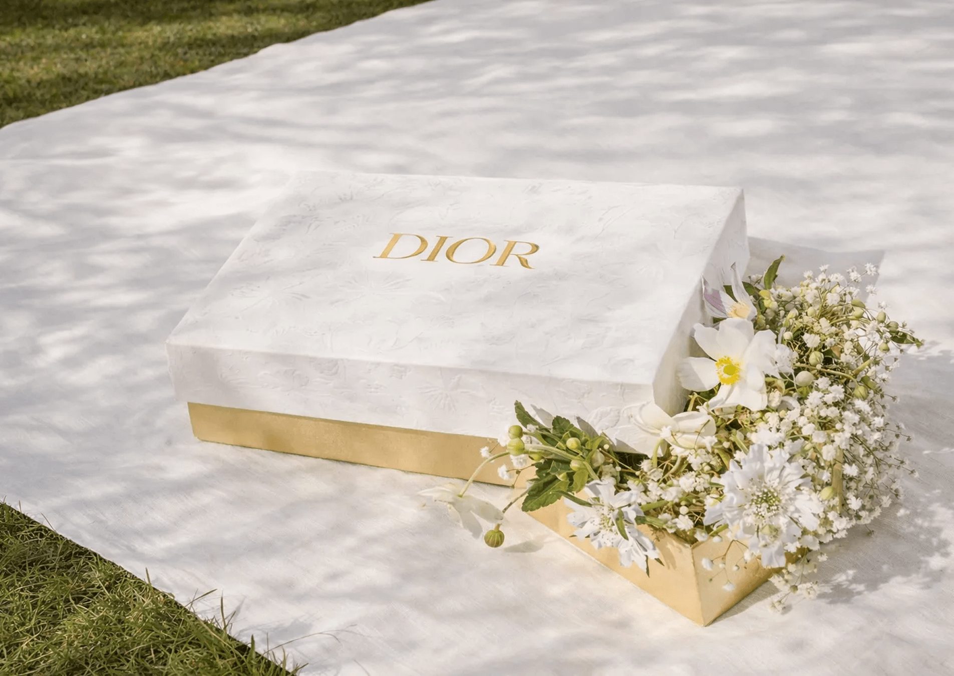 Estuche Dior con flores blancas sobre una superficie de mármol claro.