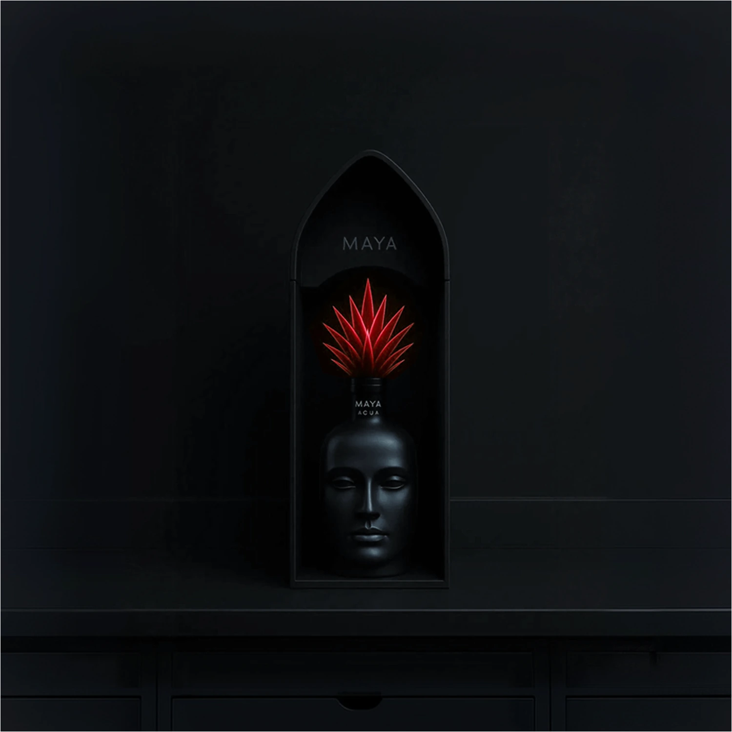 Black face-shaped Maya bottle with a red cap, displayed in a dark box with a pointed top.
