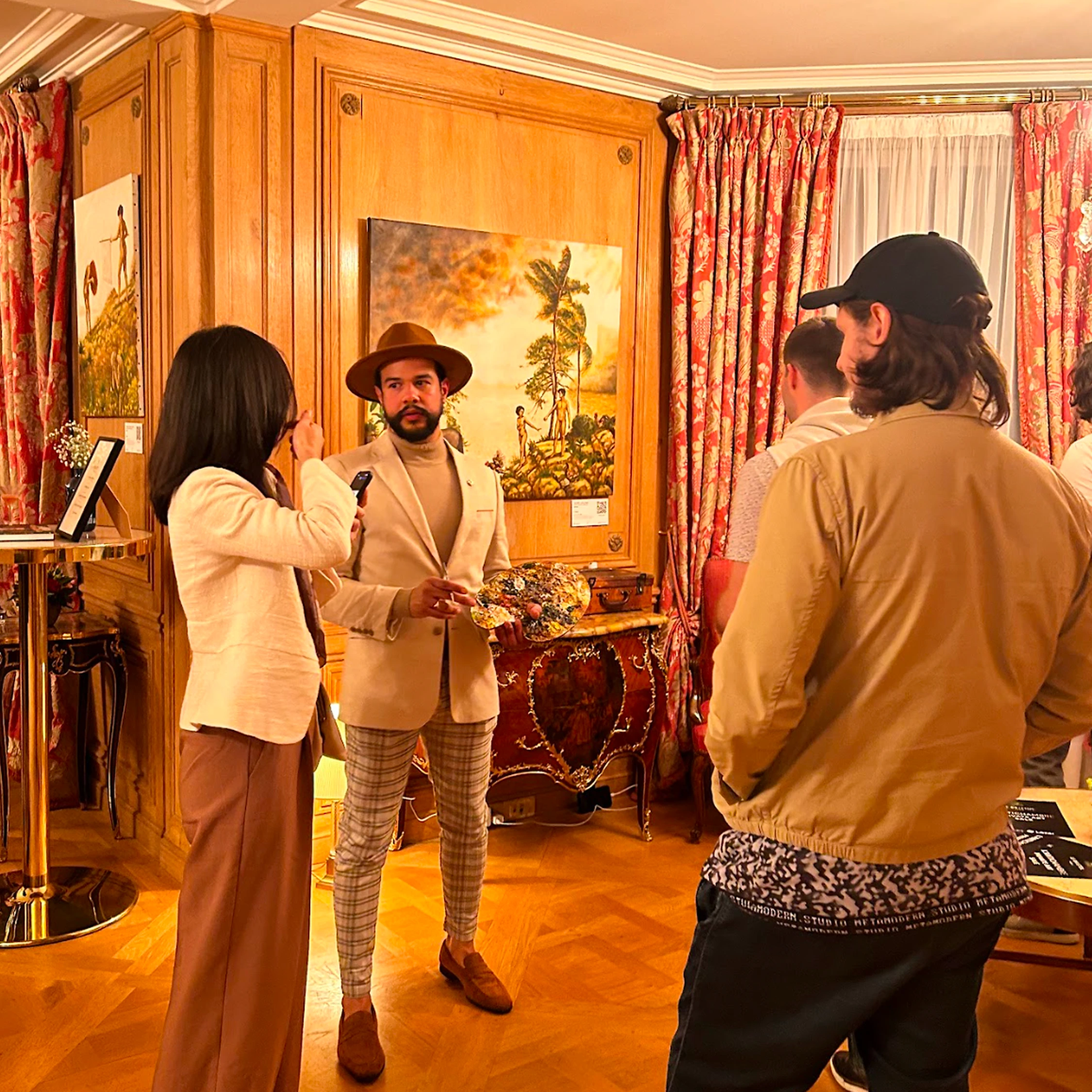 Three visitors beside paintings in a warm room with wooden wall panels.