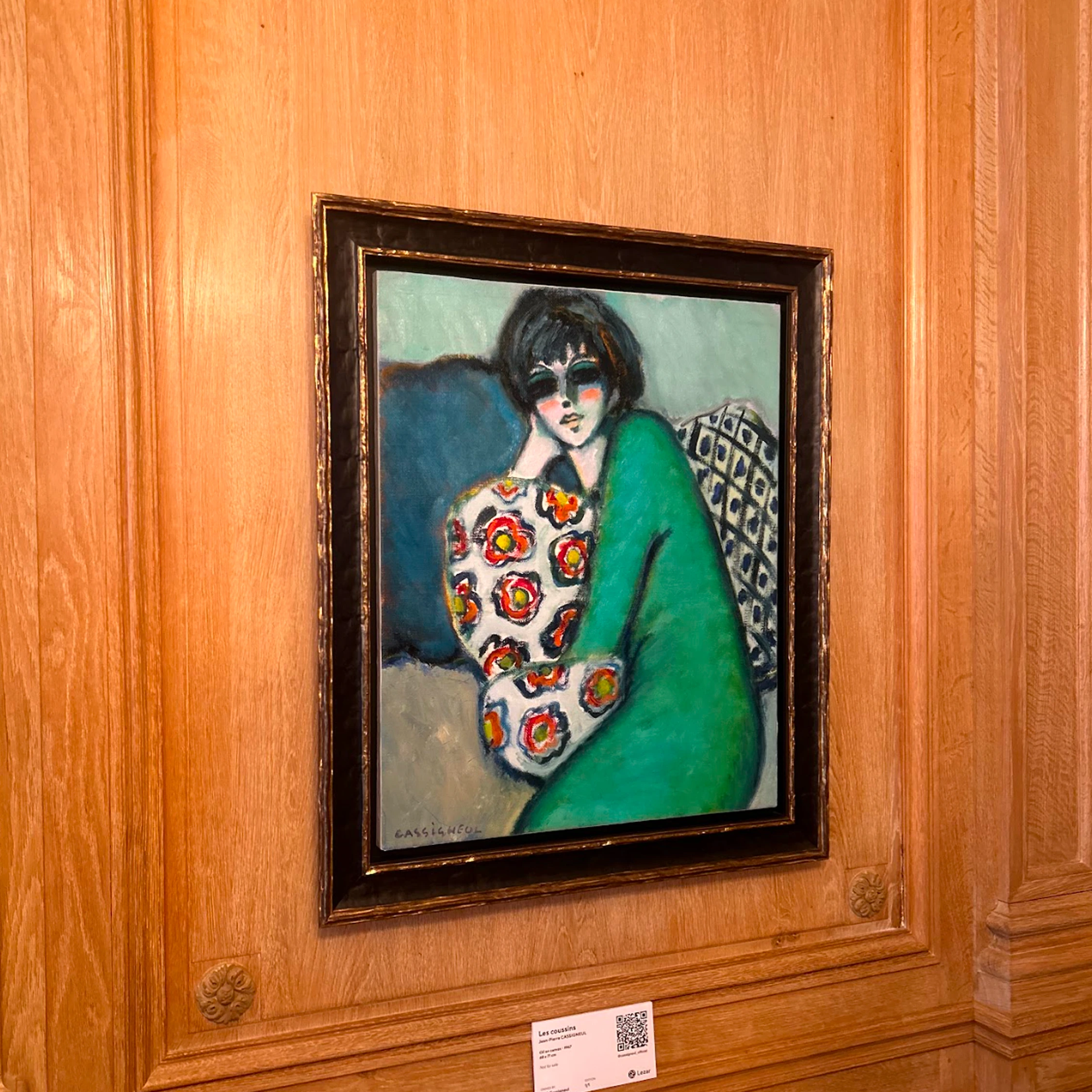 A framed portrait with a green garment hanging on a wooden wall.