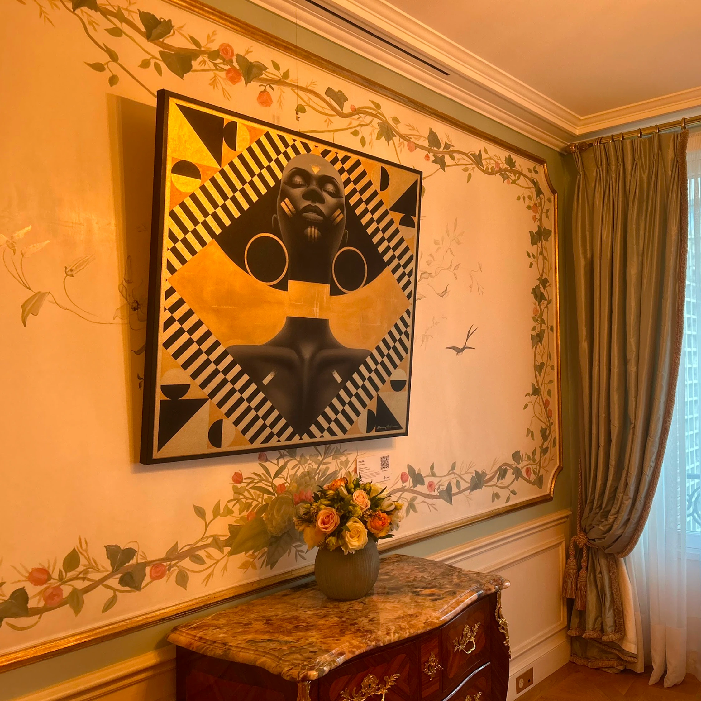 A black and gold geometric portrait above flowers in an ornate room.