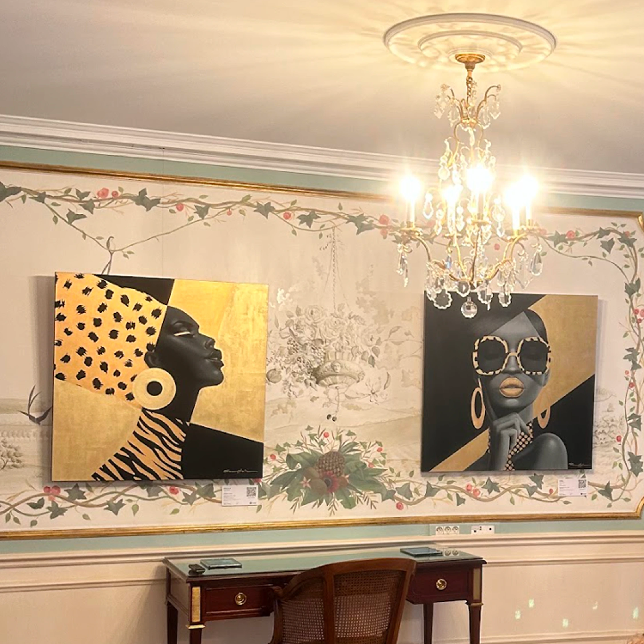 Two gold and black portraits displayed beneath a crystal chandelier.