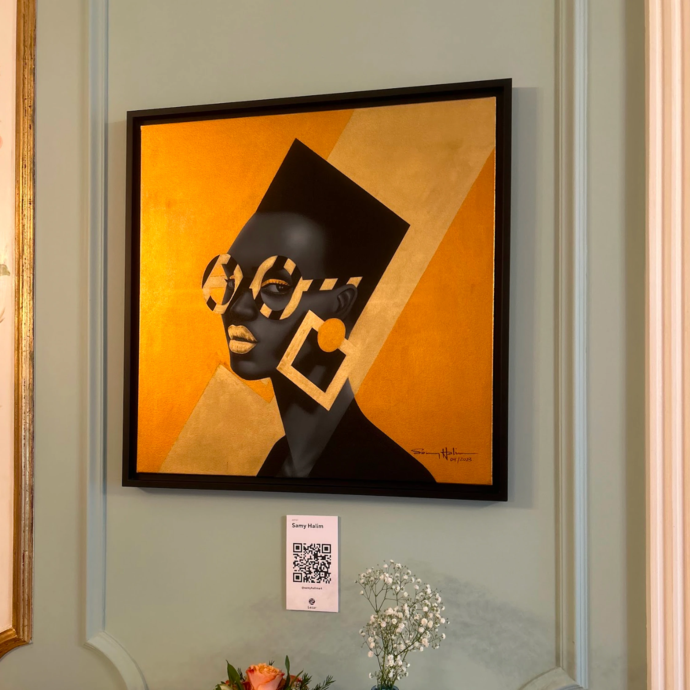 A framed gold and black geometric portrait on a pale green wall.