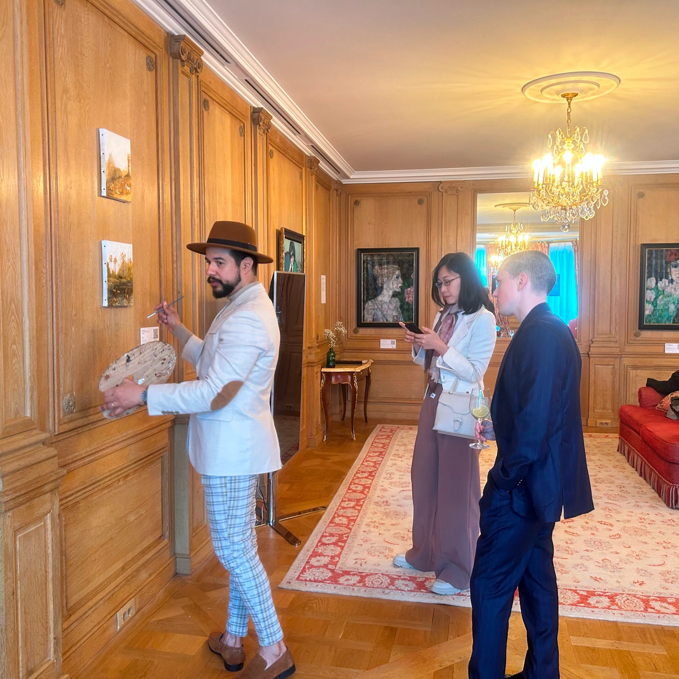 Three visitors looking at paintings in a wood-panelled salon.