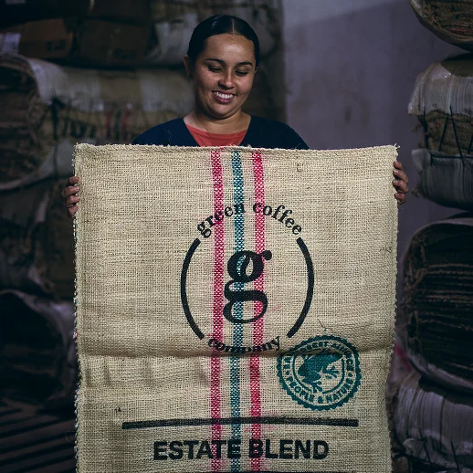 A woman holding a large brown bag with the words Green Coffee Estate Blend on it.