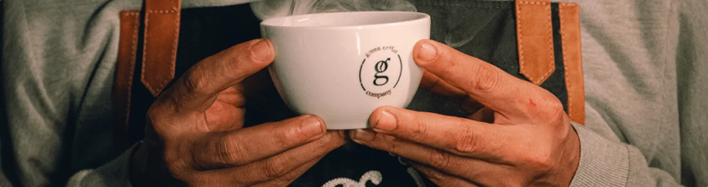 Hands holding a steaming cup with the Green Coffee Company logo.