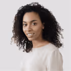 Portrait of a smiling young woman with curly black hair wearing a light beige top against a light gray background.