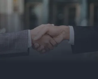 Close-up of two people shaking hands, one wearing a plaid jacket and the other a dark suit.