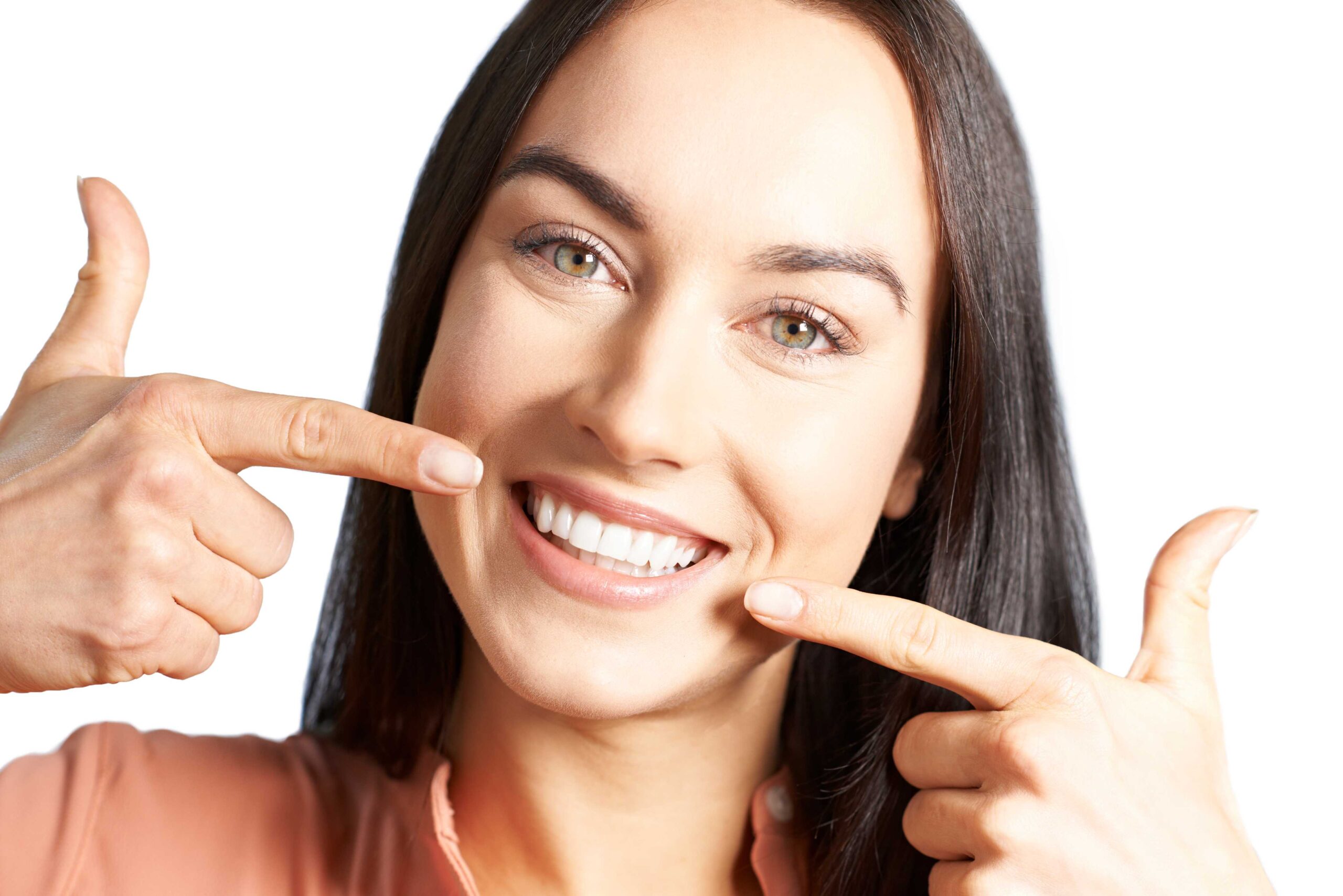 Smiling woman with brown hair pointing to her white teeth with both hands.
