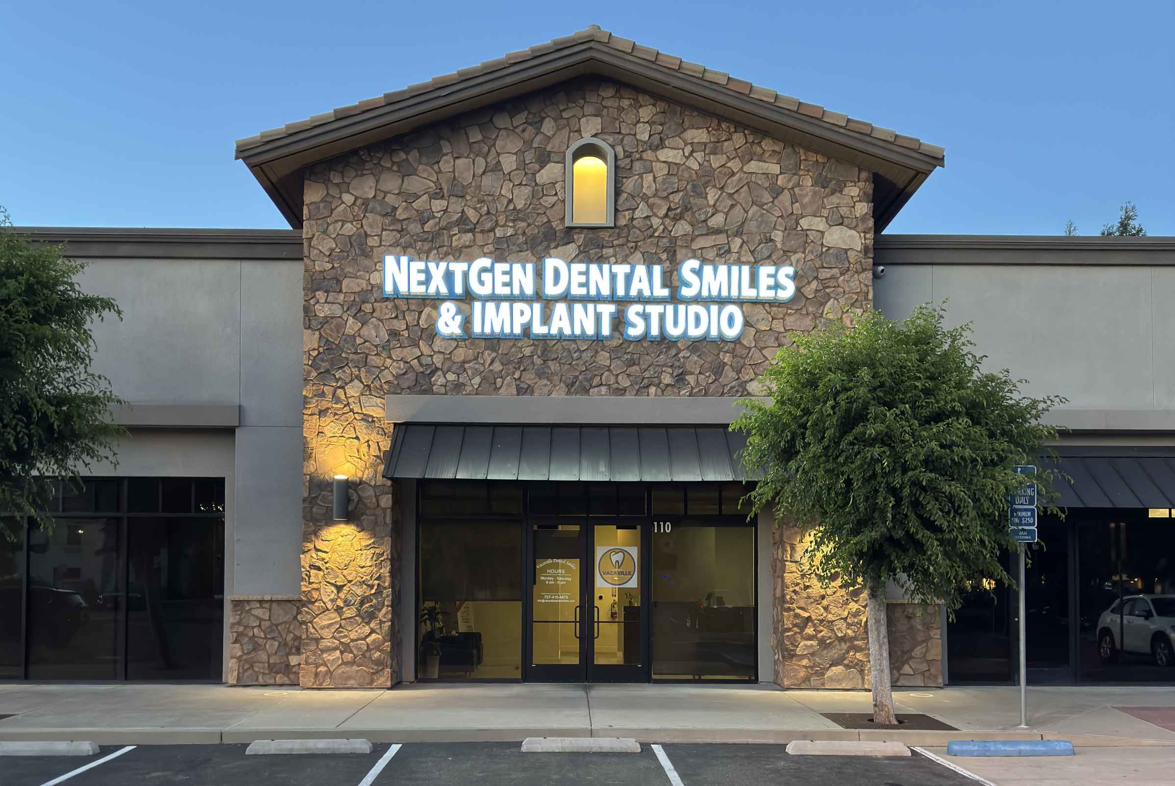Stone facade building with illuminated sign reading NextGen Dental Smiles & Implant Studio above glass entrance doors.