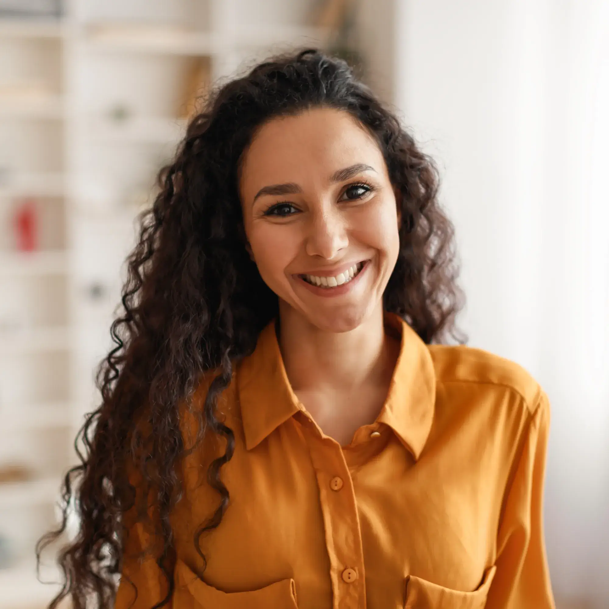 Smiling woman with long curly hair wearing a mustard yellow button-up shirt.