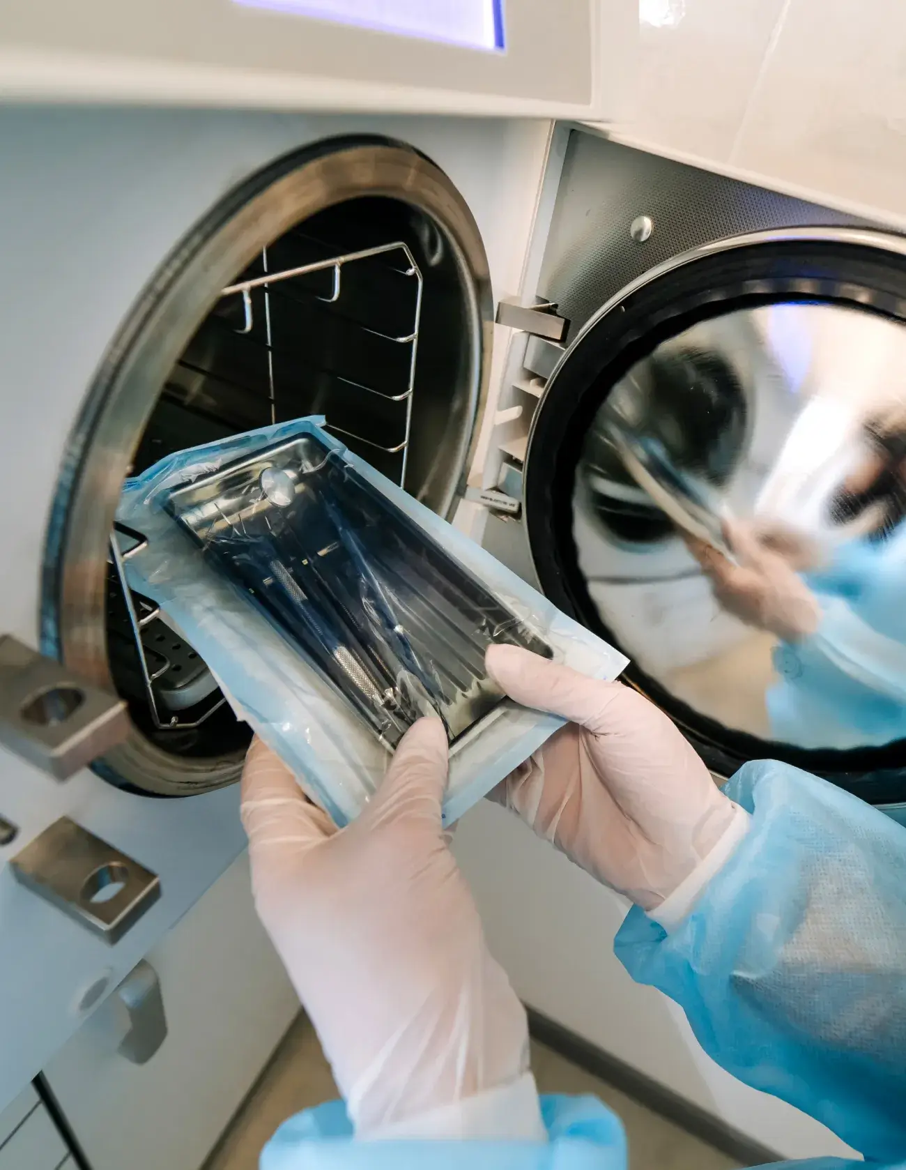 Hands in gloves placing sealed dental instruments into an autoclave sterilizer.