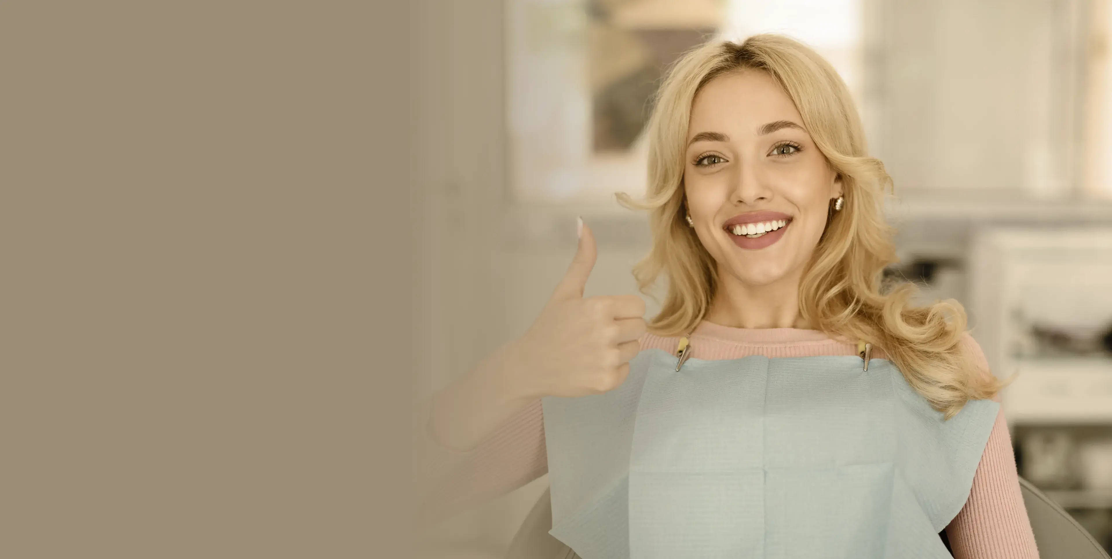 Smiling woman at a dental office wearing a dental bib and giving a thumbs-up.