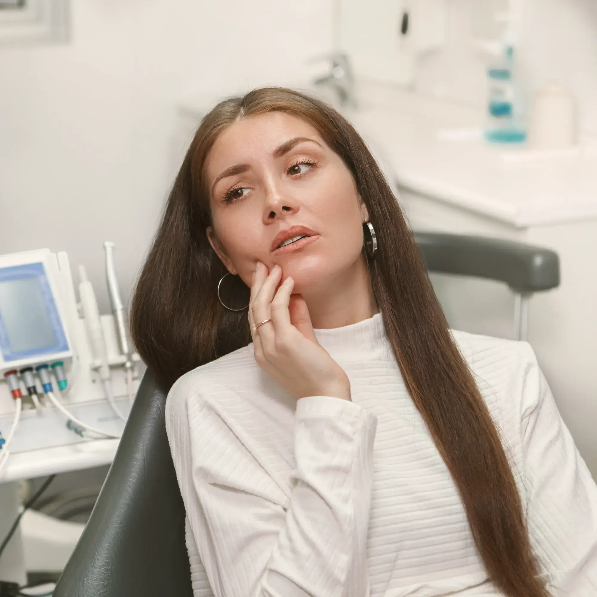 Woman sitting in a dental chair holding her cheek, appearing to have tooth pain.
