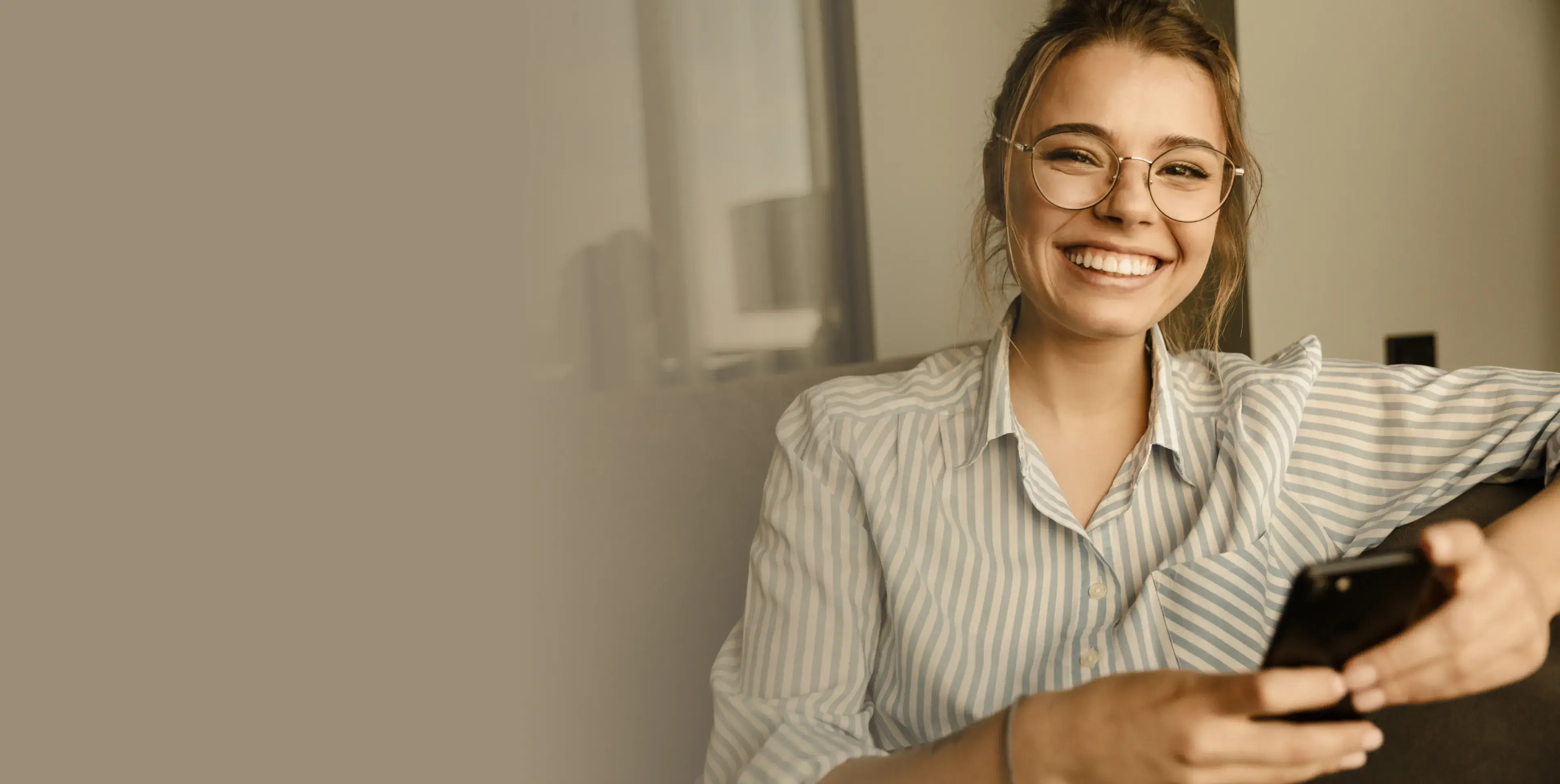 Smiling woman wearing glasses and a striped shirt holding a smartphone.