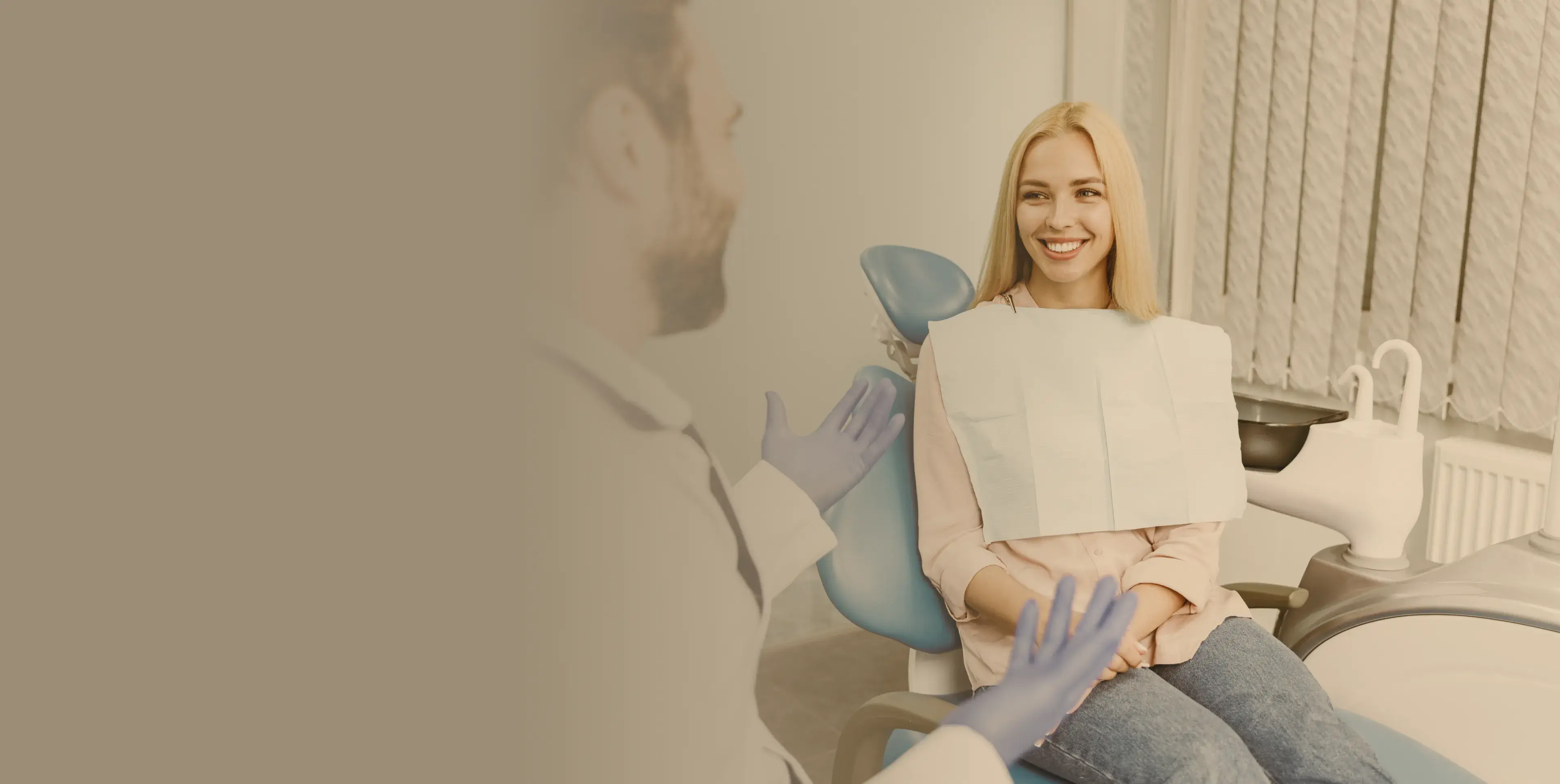 A female patient sitting in a dental chair smiling while talking to a dentist wearing gloves.