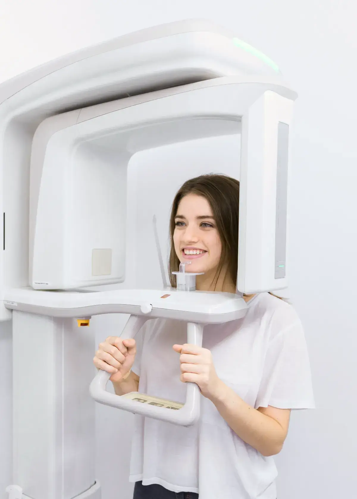 Young woman smiling while undergoing a dental panoramic X-ray scan using a large white imaging machine.