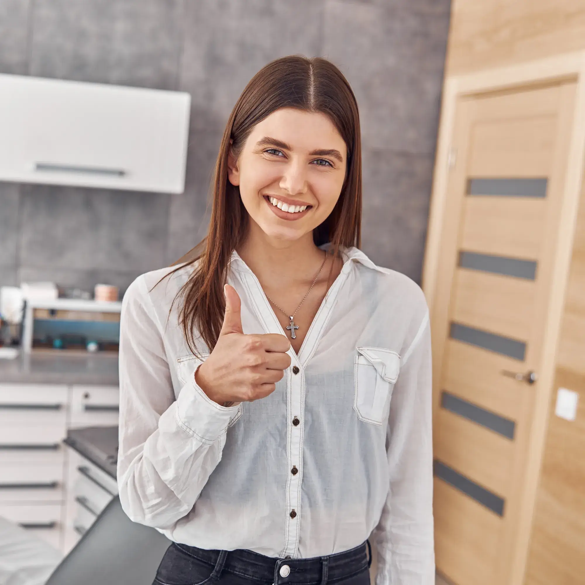 Smiling woman in white shirt giving a thumbs up while standing in a modern kitchen.