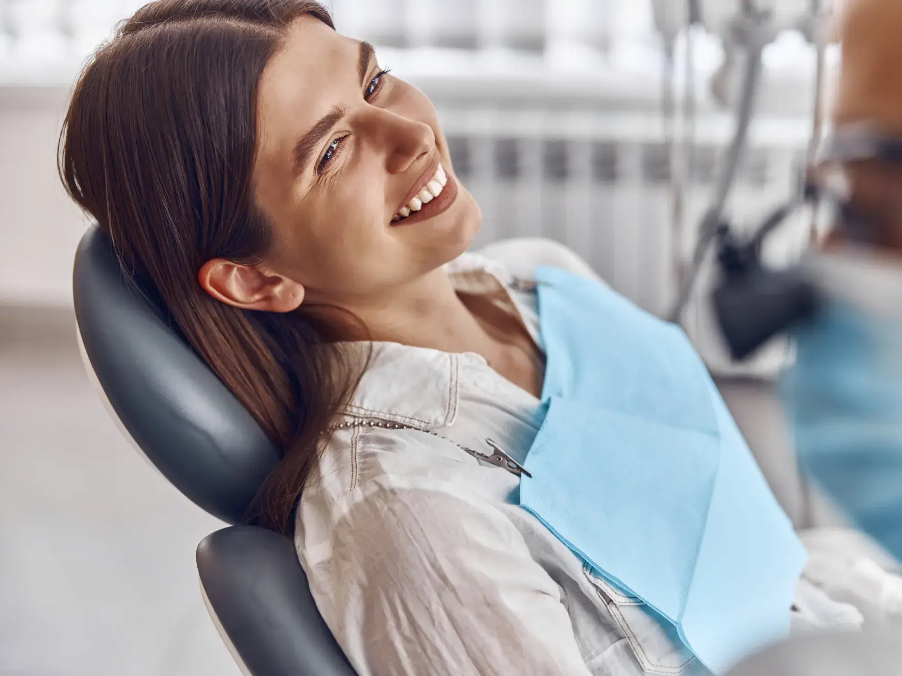 Smiling woman reclining in a dental chair wearing a blue dental bib.