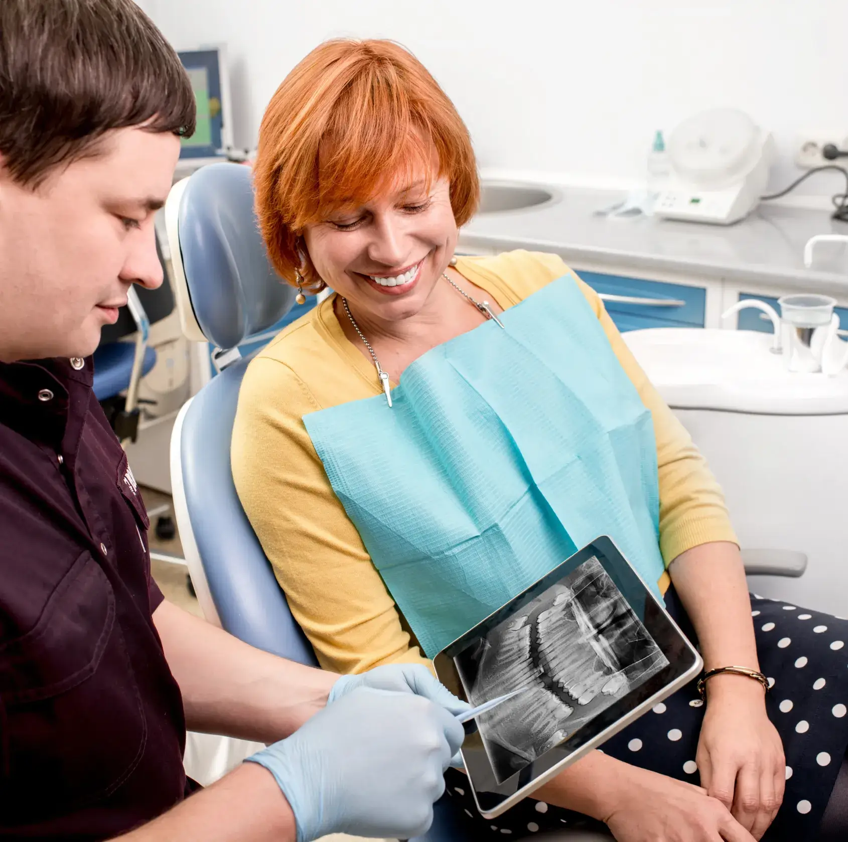 Dentist showing a dental x-ray on a tablet to a smiling woman sitting in a dental chair.