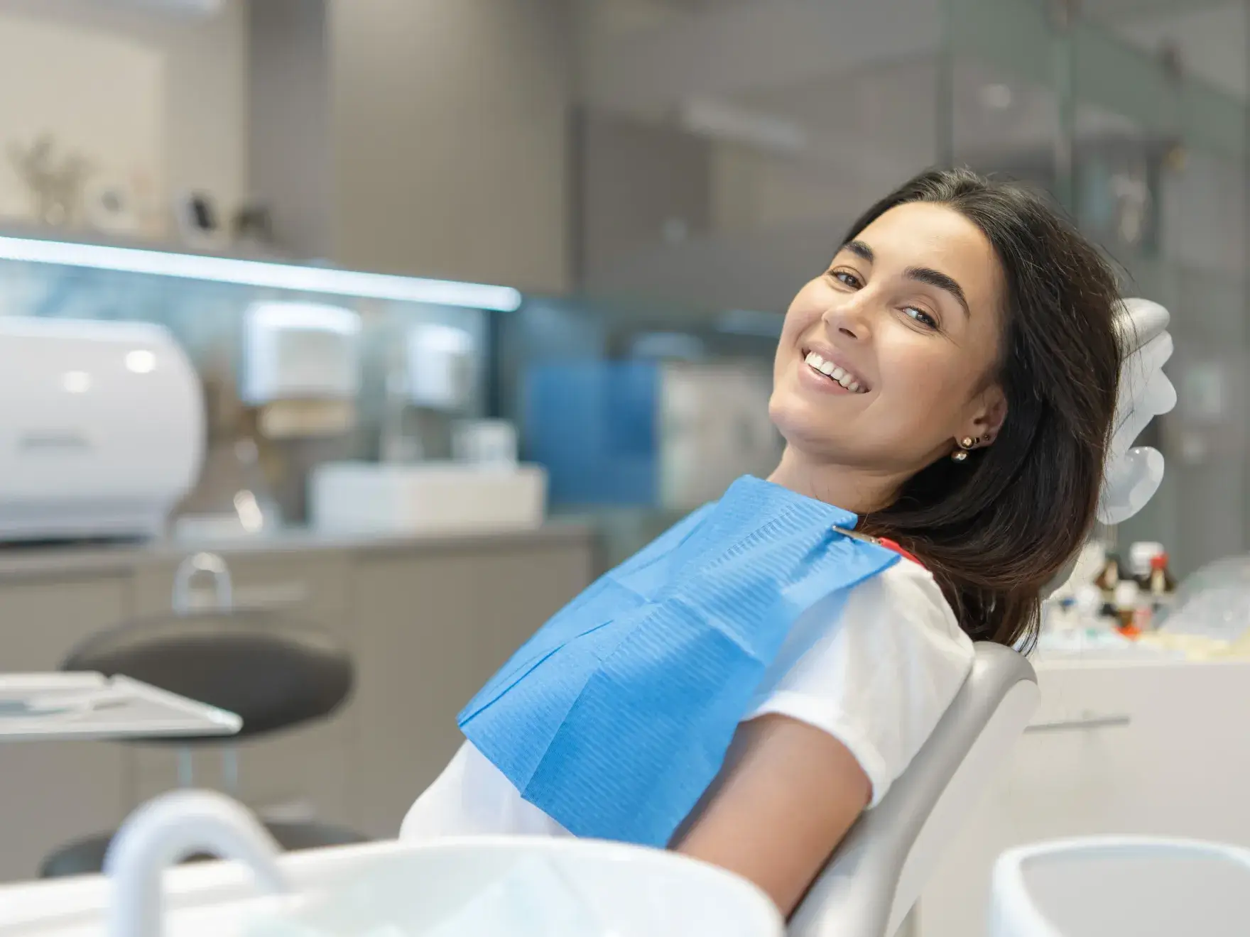 Smiling woman wearing a dental bib sitting in a dental chair in a modern clinic.