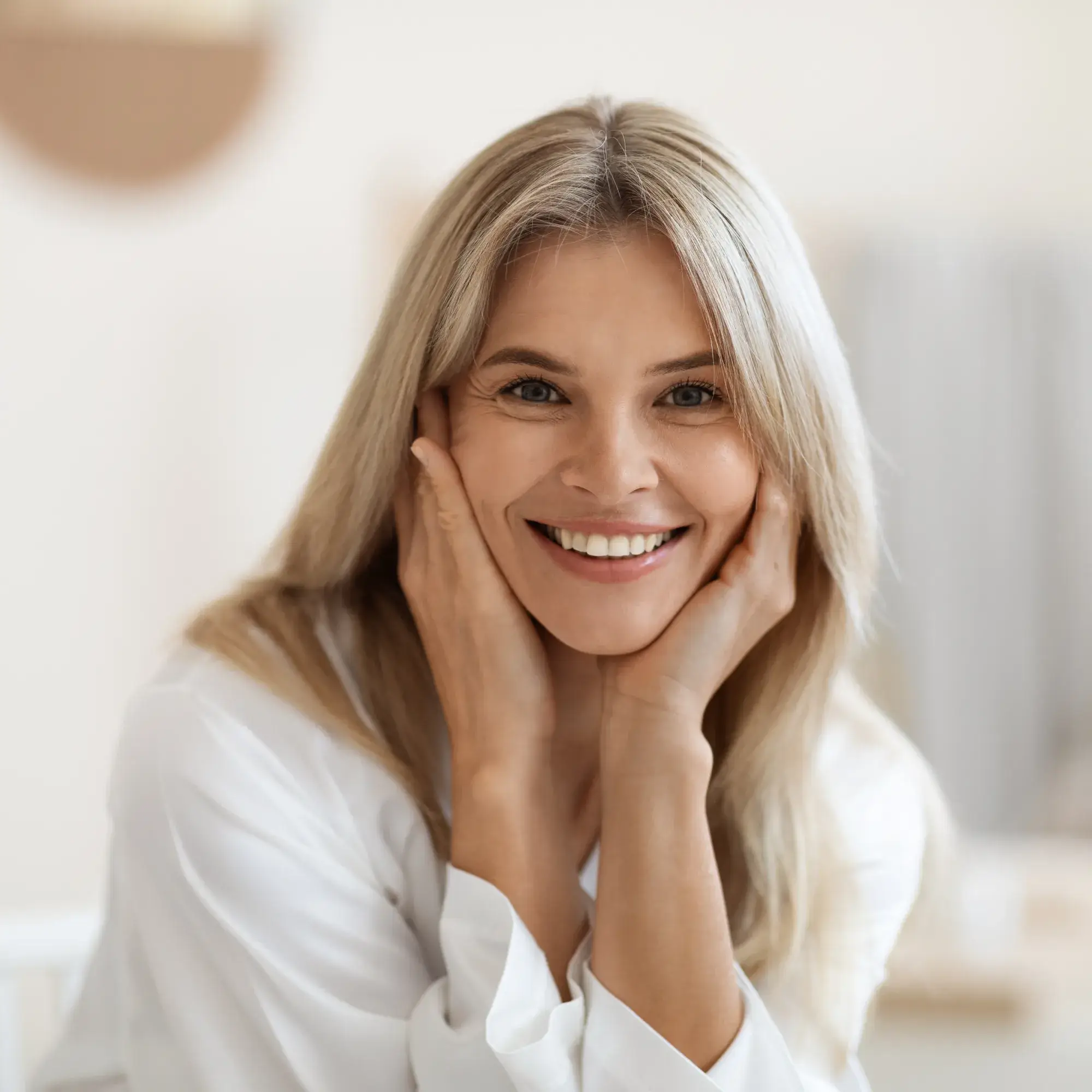 Smiling middle-aged woman with blonde hair resting her face in her hands.
