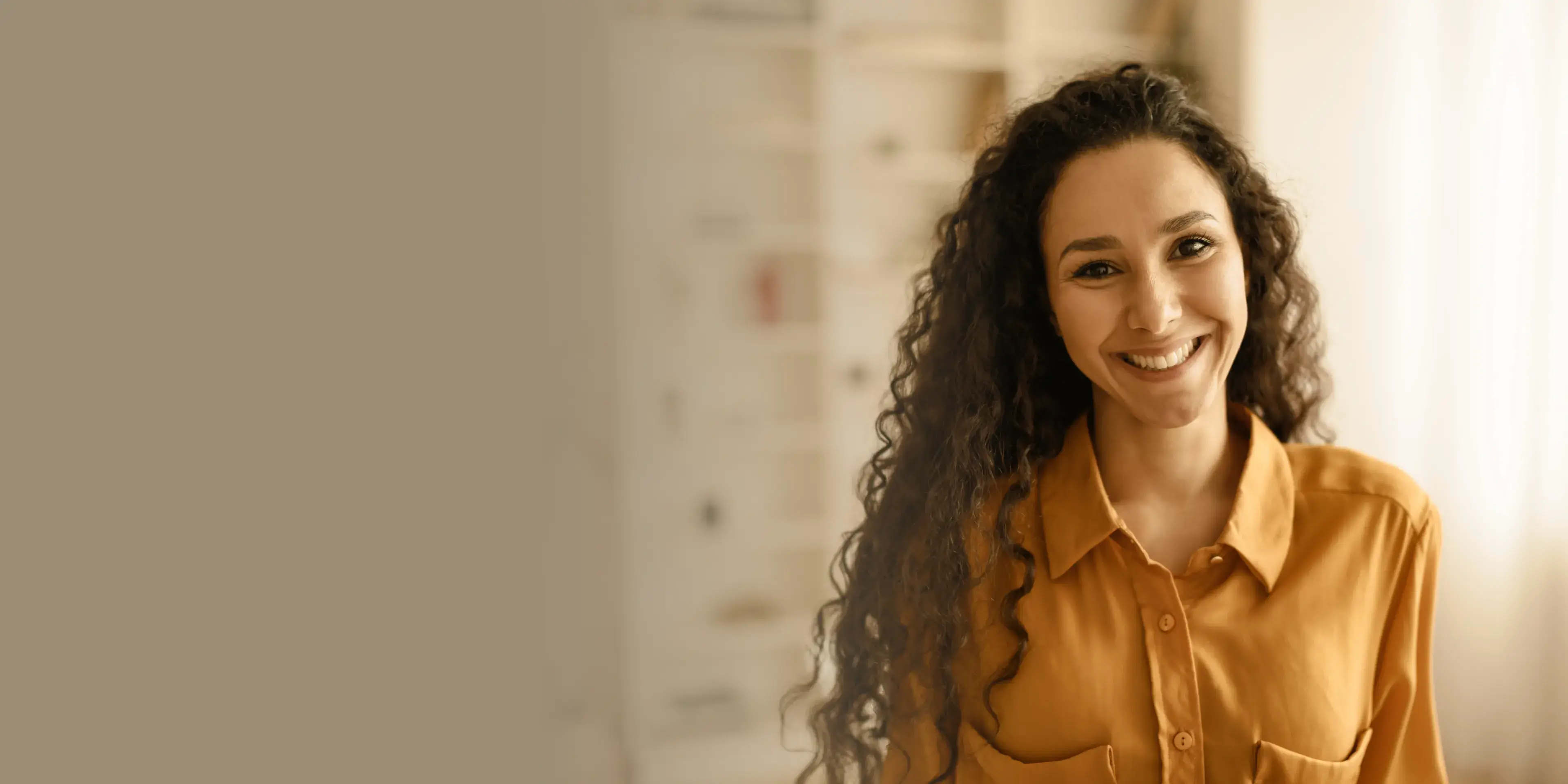 Smiling woman with long curly hair wearing a mustard yellow button-up shirt.