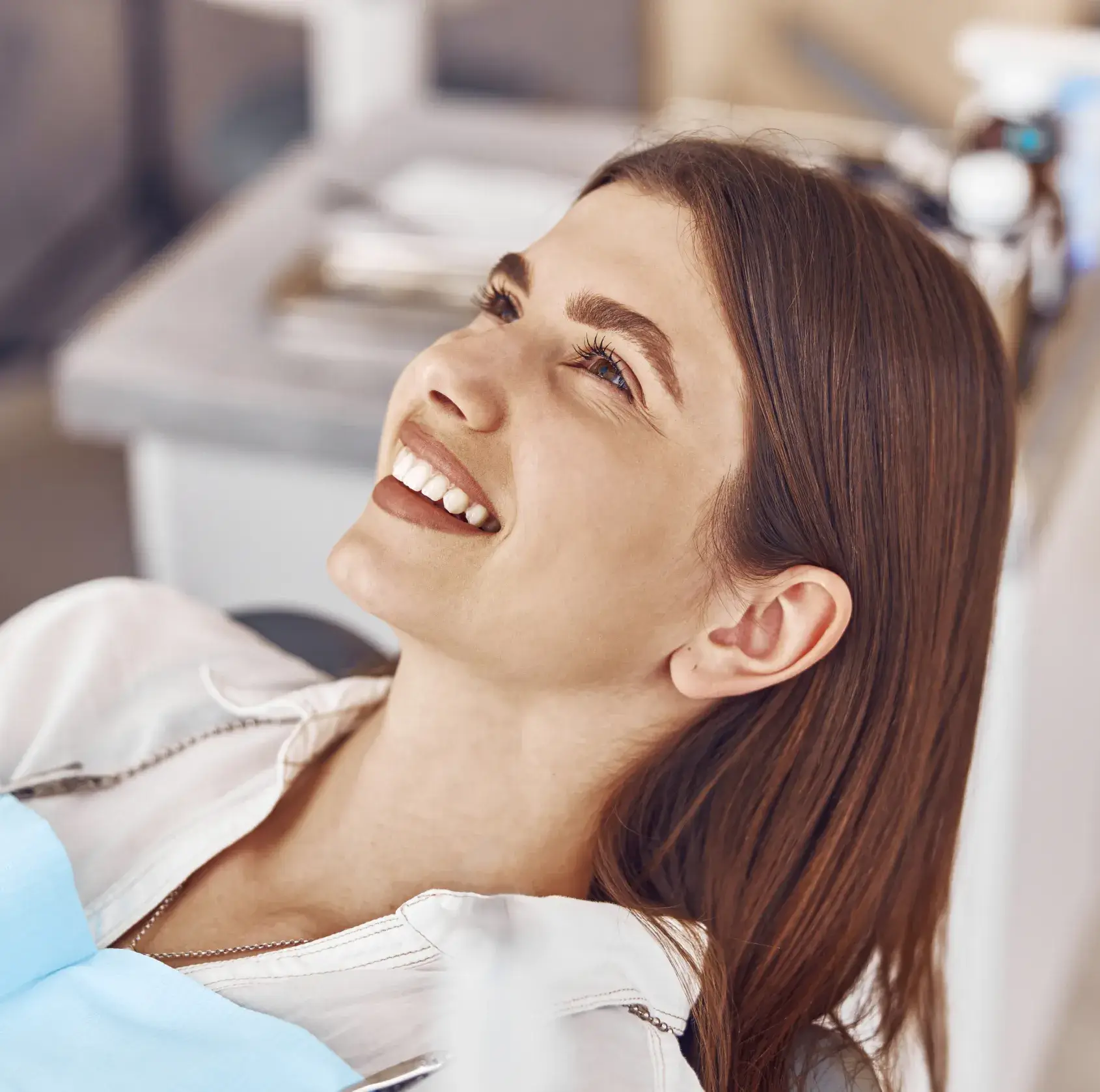 Smiling woman with brown hair reclining in a dental chair wearing a blue dental bib.
