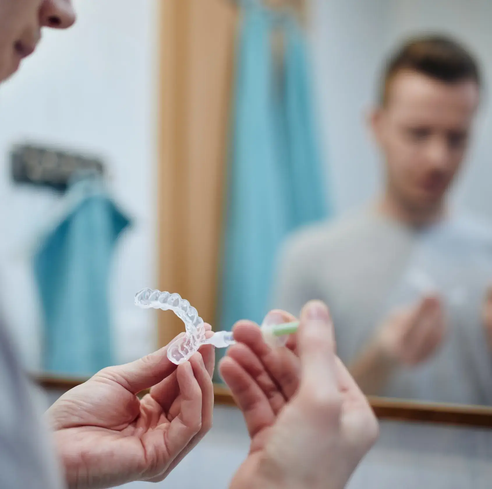 Person applying whitening gel to a clear dental tray in front of a bathroom mirror.