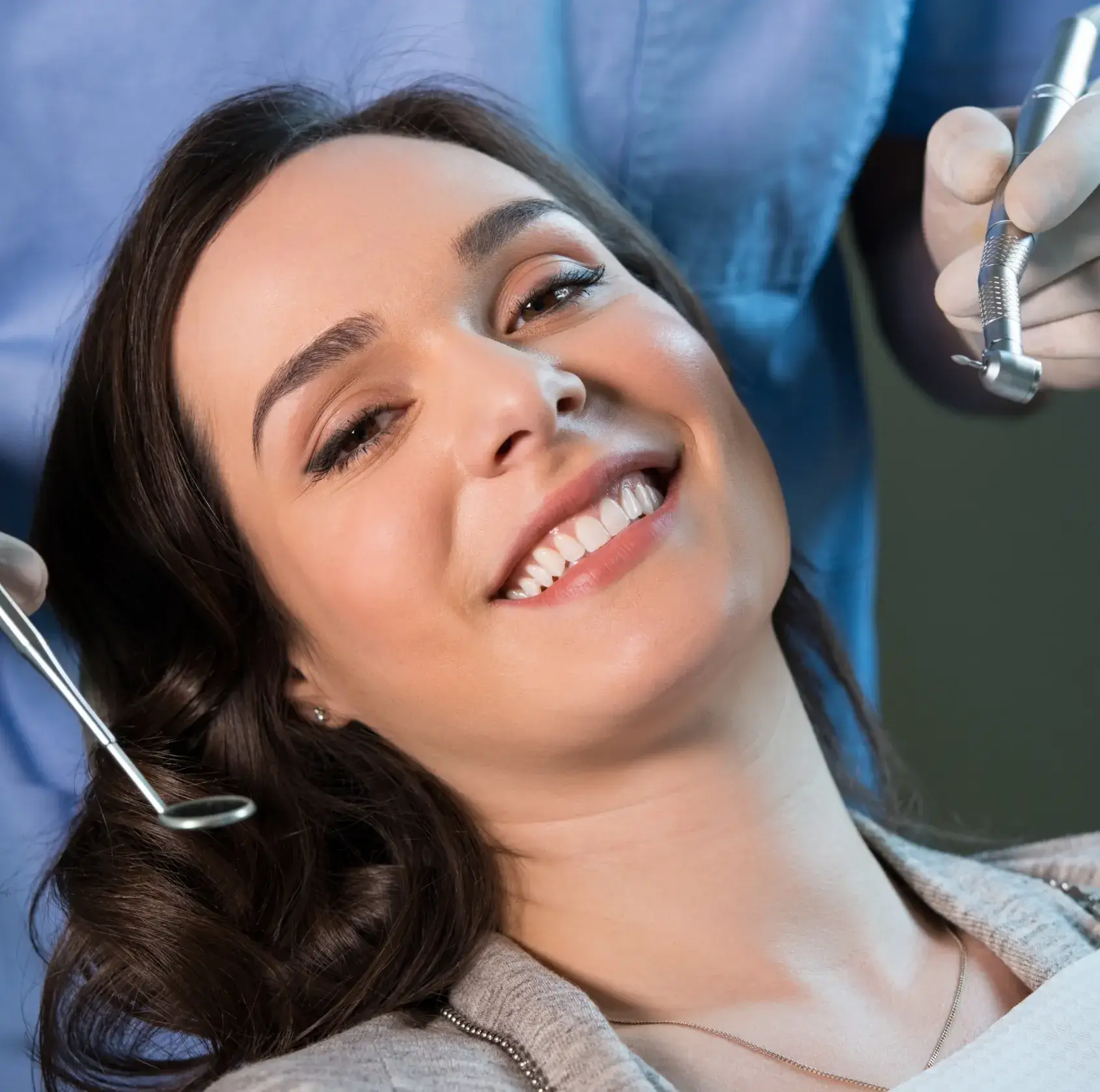 Smiling woman reclining in a dental chair with dental tools near her, ready for a cleaning.