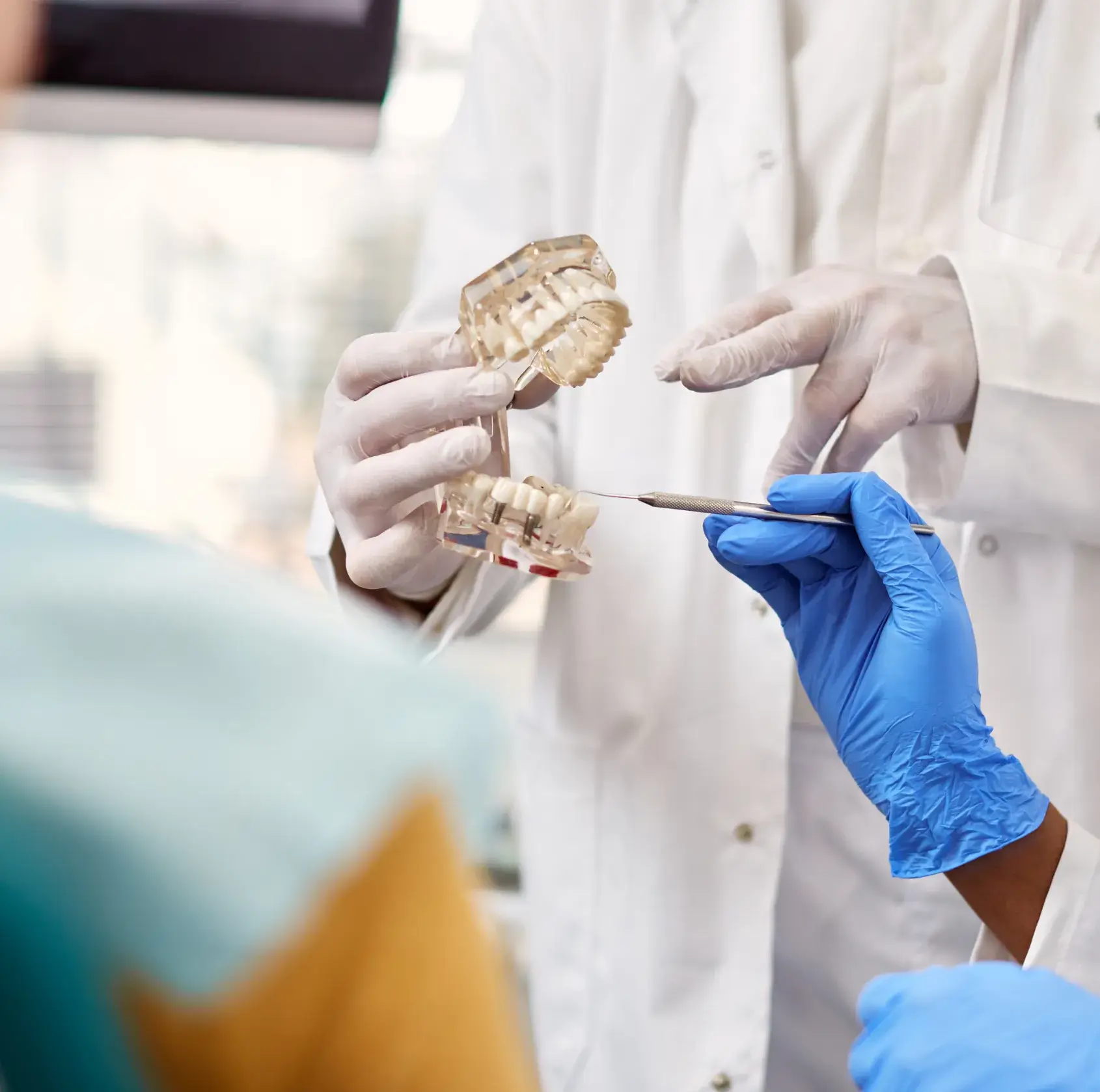 Dental professionals wearing gloves examining a dental model with a tool.