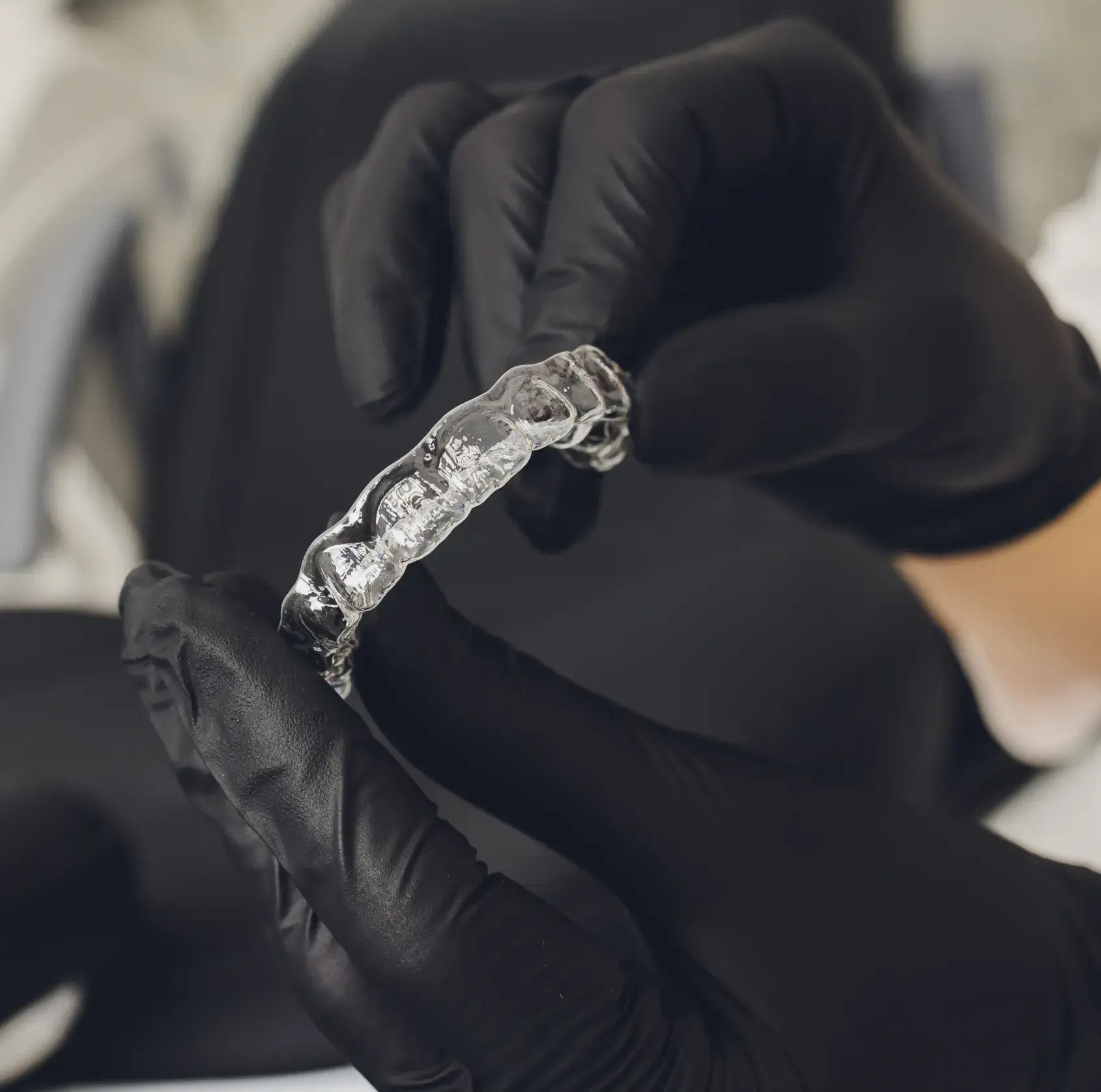 Gloved hands holding a clear dental aligner against a dark background.