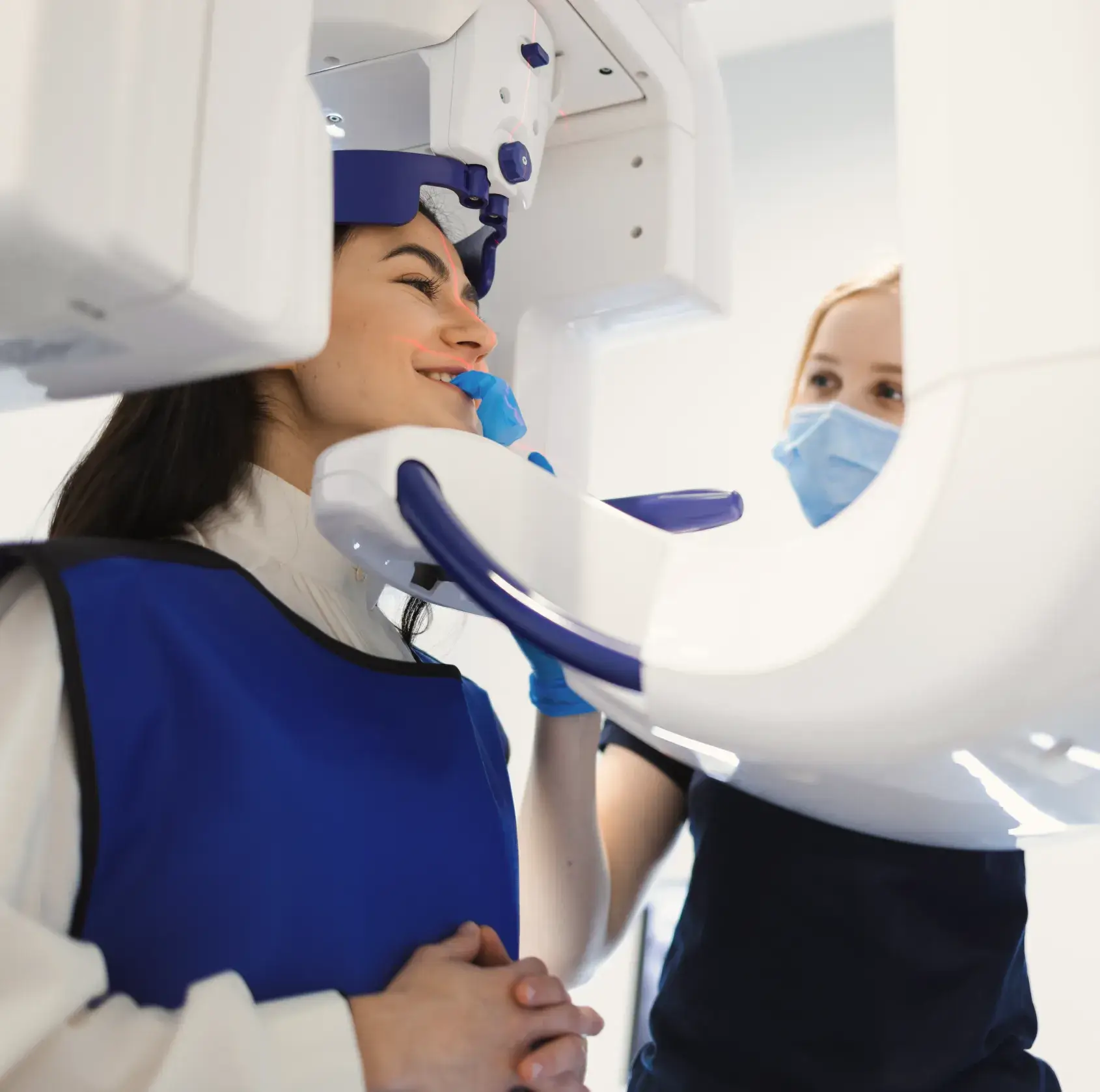 Patient wearing a protective apron getting a dental X-ray with a technician assisting in a clinical setting.