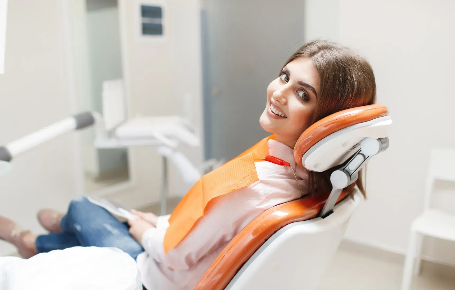 Smiling woman sitting in a dental chair wearing an orange protective bib in a dental office.