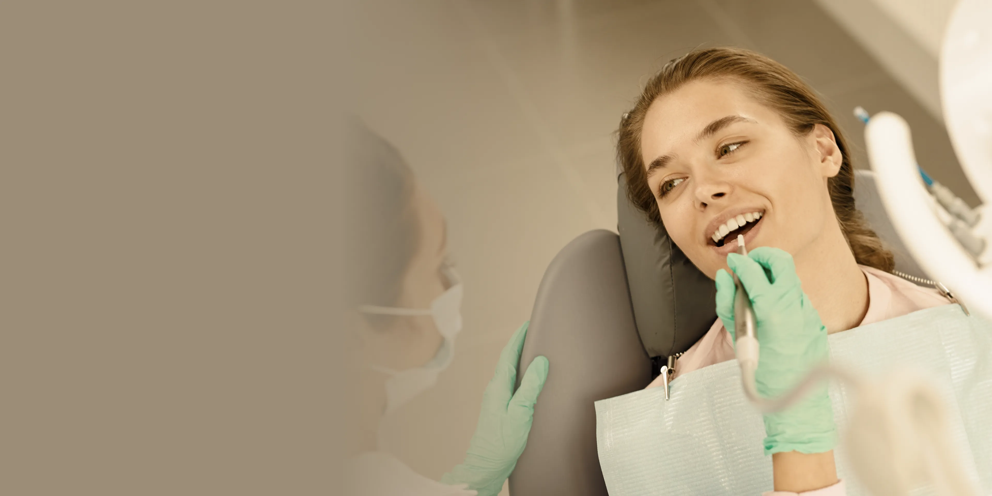 Dentist wearing gloves and a mask examining a smiling female patient's teeth in a dental chair.