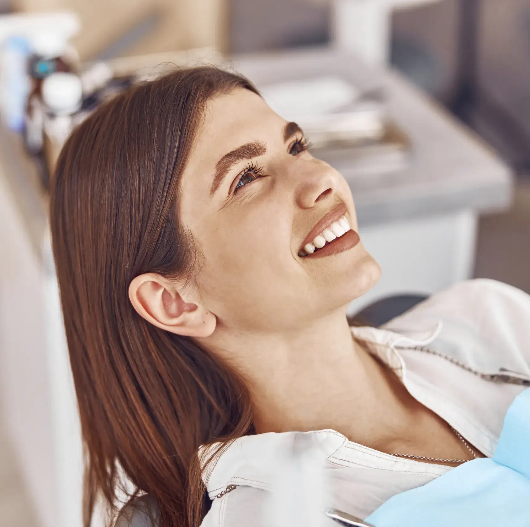 Young woman with brown hair reclining in a dental chair, smiling and looking upward.