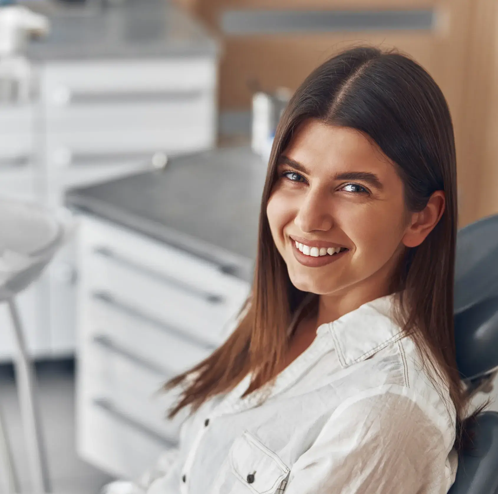 Smiling young woman with long brown hair sitting in a dental clinic chair.