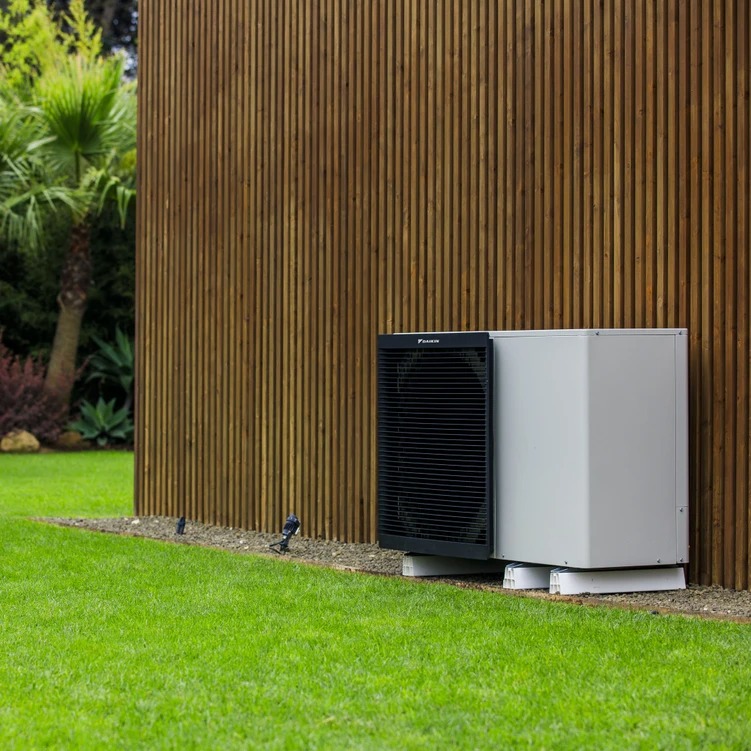 Modern air conditioning unit installed against wooden slat exterior wall on green lawn.