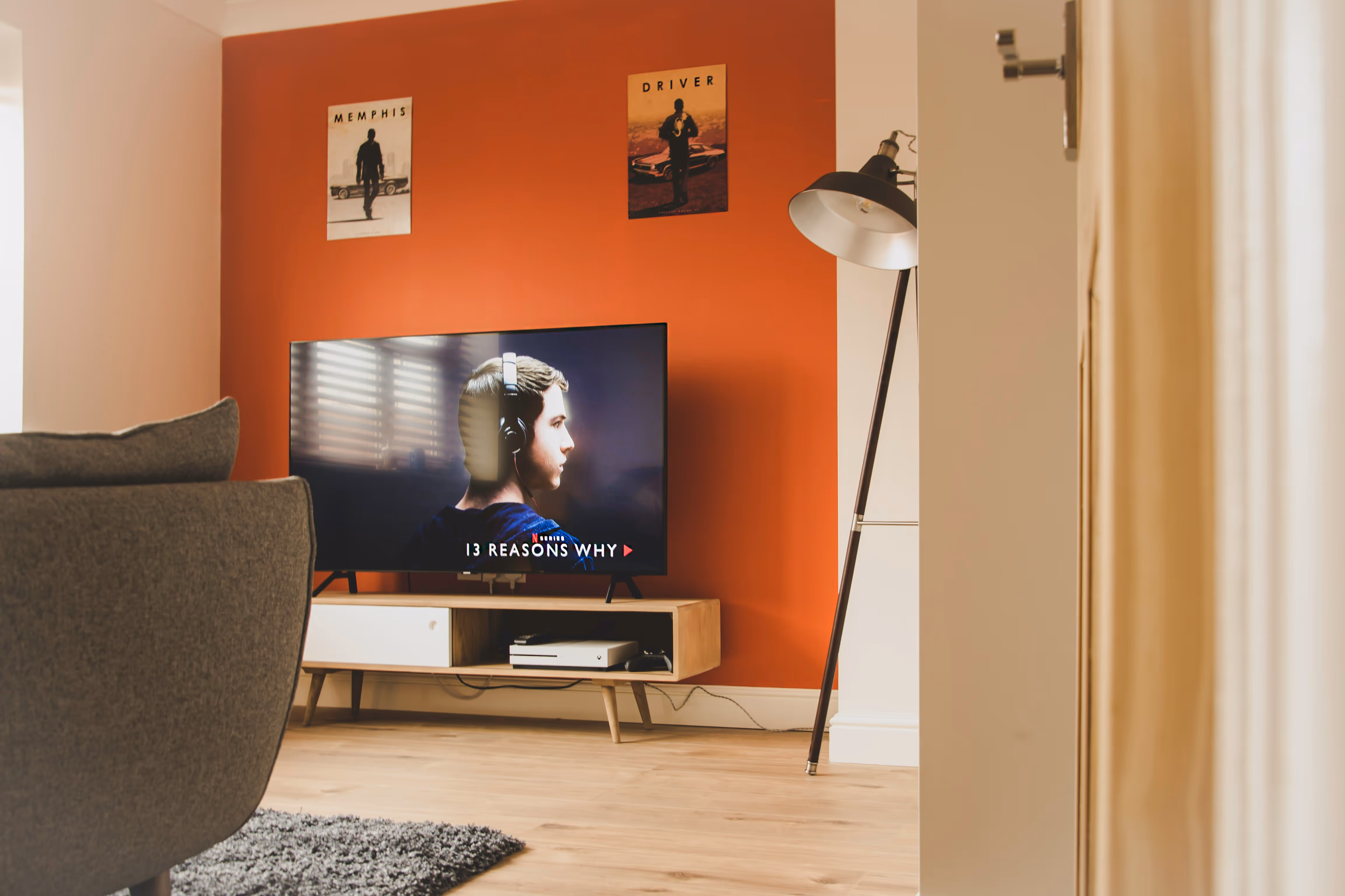 TV showing 13 Reasons Why on a wooden stand in a living room with red accent wall and posters