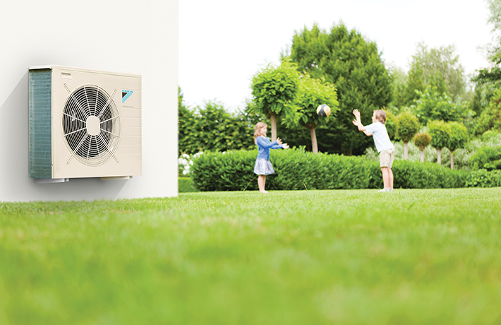 Two children playing with a ball outside near a white wall with an air conditioning unit.